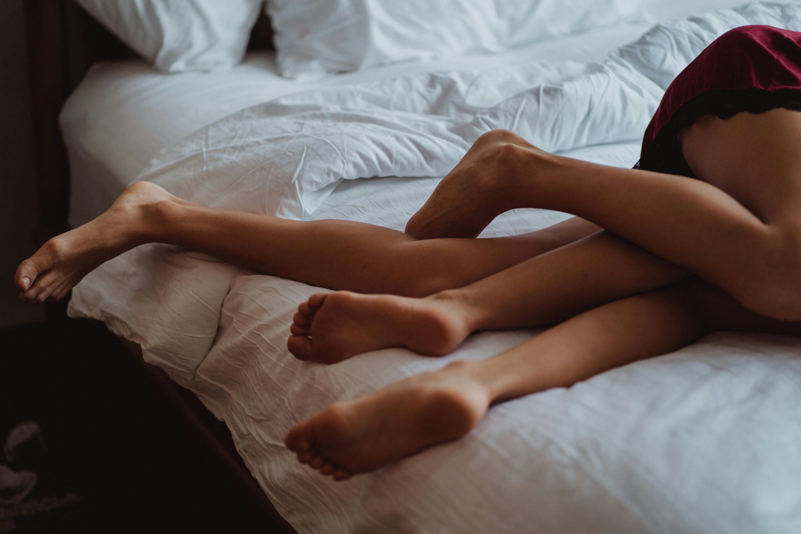the legs of 2 lovers intertwined, sideways on a bed with white sheets